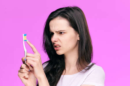 Beautiful young woman on a pink background holds a toothbrush.の写真素材