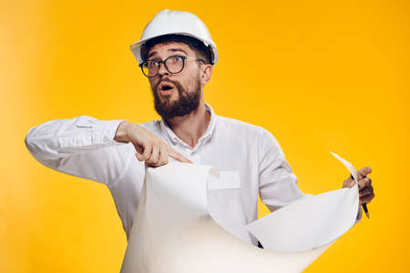 Engineer with a beard on a yellow background holds blueprints.の写真素材