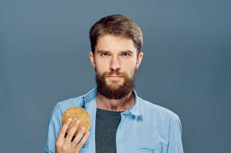 Man with a beard on a gray background holds a hamburger, bad food.の写真素材