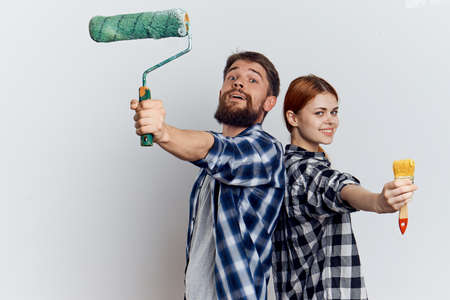 Man with a beard on a light background with a young beautiful woman holding construction tools, repairing.の写真素材