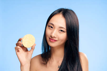 Young beautiful woman on a blue background holds a sponge for make-up removal, asian, beauty.の写真素材
