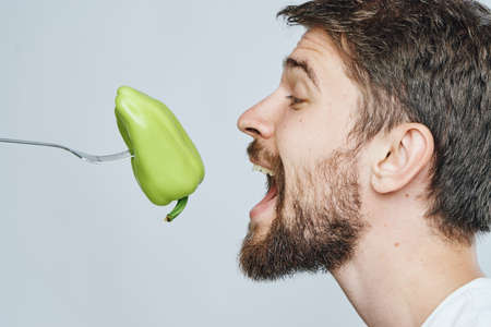 Man with a beard on a white isolated background mouths pepper, vegetables, diet, vegetarianism.の写真素材