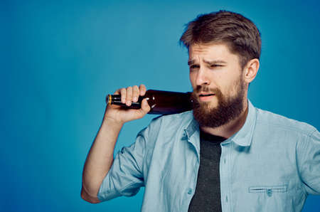 Man with a beard on a blue background holds a bottle of beer, alcohol.の写真素材
