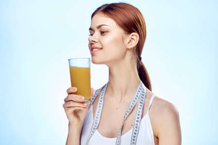 Young beautiful woman on a blue background holds a glass of fresh orange juice, health, diet.の写真素材
