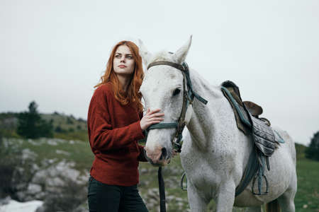 Young beautiful woman walking in the mountains with a white horse.の写真素材