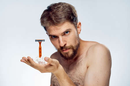 Man with a beard on a white isolated background holds a shaving foam and a razor.の写真素材