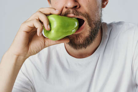 Man with a beard on white isolated background eating fresh pepper, vegetables, diet, vegetarianism.の写真素材