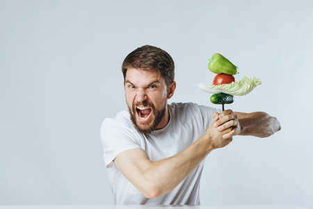 Man with a beard on a light background holds vegetables and screams, vegetarianism, diet.の写真素材