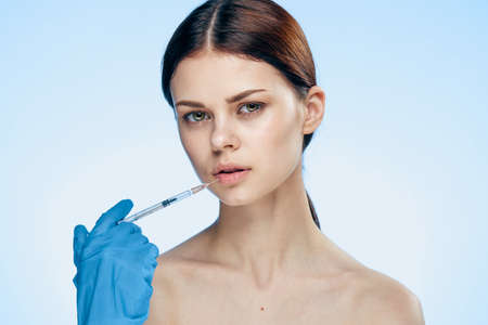 Young beautiful woman on a light blue background holds a syringe, medicine, plastic surgery.の写真素材