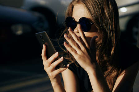 Young beautiful woman in sunglasses outside in the city holding a phone.の写真素材