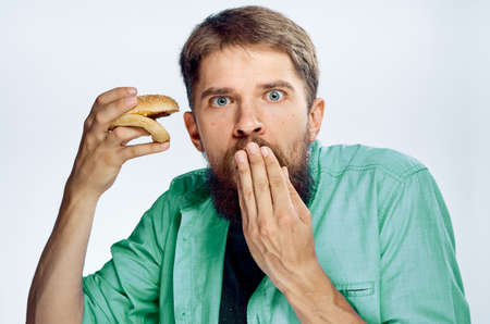 Man with a beard on a white isolated background holds a hamburger, emotions, fast food.の写真素材