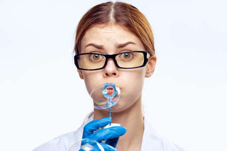Young beautiful woman on white isolated background in medical dressing gown and gloves blowing bubbles, medicine, doctor.の写真素材