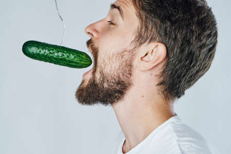 A man with a beard on a light background eating a cucumber, vegetables.diet, a vegetarian.の写真素材
