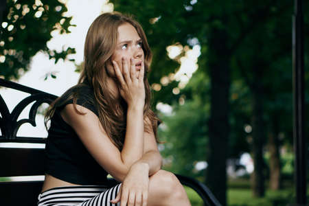 Young beautiful woman sits on a bench outdoors in summer park.の写真素材