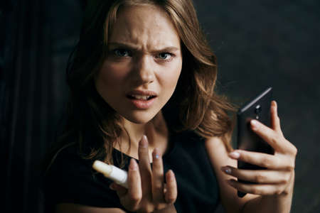 Young beautiful woman holding a phone and a hygienic lipstick.の写真素材