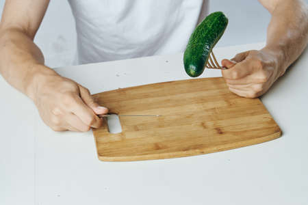Man sitting at a table, cucumber on a cutting board, white background.の写真素材