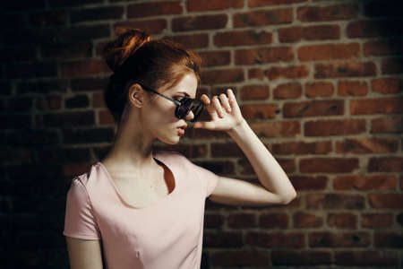Young beautiful woman in sunglasses against the backdrop of a brick wall.の写真素材