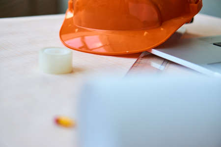 Orange construction helmet on the table, adhesive tape, paper for drawings.の写真素材