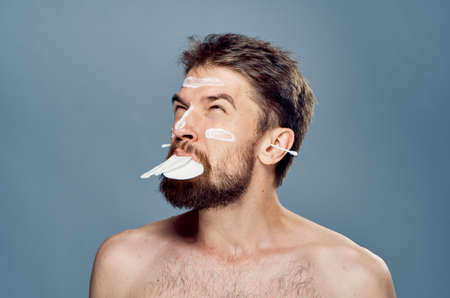 A man with cotton pads in his mouth, cream on his face and ear wands in his ears on a gray background.の写真素材