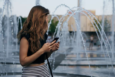Young beautiful woman walking outdoors in city in summer at fountain.の写真素材