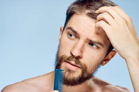 A man with a beard on a blue background holds a comb, a hairdo.の写真素材