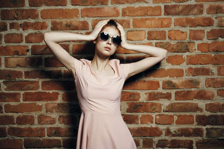 Young beautiful woman in sunglasses holds on to the head near the kerp wall.の写真素材