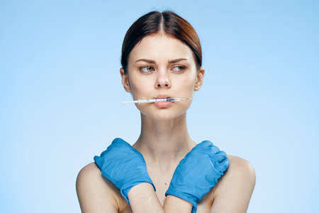 Beautiful woman holding a syringe in her mouth on a blue background, medical gloves, botox.