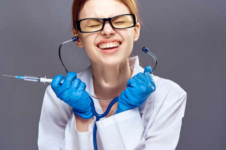 Young beautiful woman on gray background with glasses and medical dressing gown drains syringe and stethoscope, medicine, doctor.の写真素材
