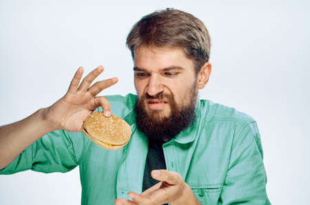 Man with a beard on a white isolated background holds a hamburger, emotions, fast food.の写真素材