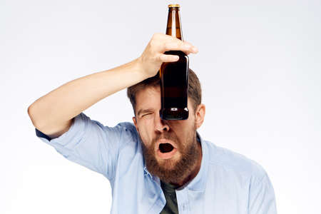 A man with a beard holds a bottle of beer near his eye a second eye closed on a light background.の写真素材