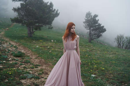 Young beautiful woman in a long blue dress in the mountains near the trees.の写真素材