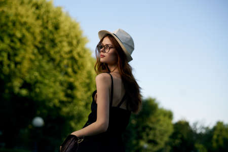 Woman in a hat and glasses on the background of a tree walking down the street.