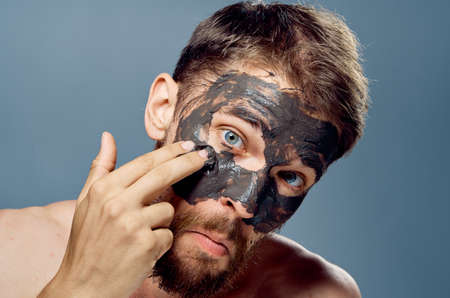 A man with a beard on a gray background applies clay cosmetic face mask, beauty, health.の写真素材