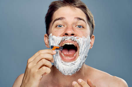 Man with a beard on a gray background shaves, portrait.の写真素材