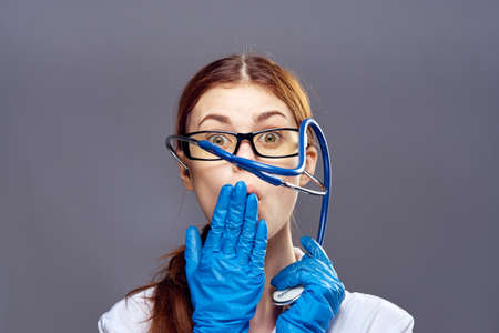 Young beautiful woman on gray background wearing glasses and medical gown, portrait, emotions, doctor, medicine.の写真素材