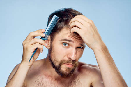 Man with a beard combs his hair on a blue background.の写真素材