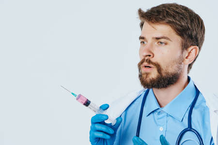Doctor with a beard holds a syringe with a substance on a light background.の写真素材