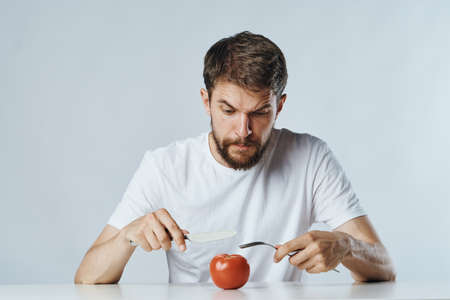 A man with a beard cuts a tomato, food restrictions, a vegetable diet.