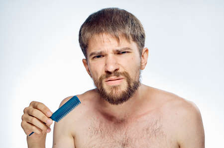 Man with a beard on a white isolated background holds a comb, emotions, hairstyle.