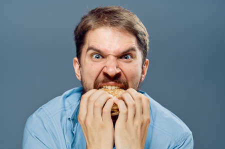 Man with a beard on a gray background eating a hamburger, emotions, portrait, fast food.