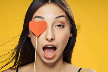 Young beautiful woman on yellow background holds paper accessories for parties, portrait, emotions.
