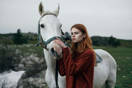 Young beautiful woman with a white horse in the mountains outdoors.