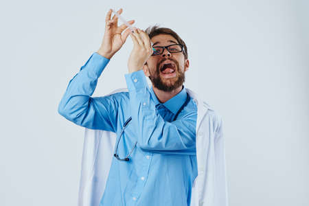 Man with a beard on a white isolated background in a medical dressing gown and wearing glasses holds a syringe, emotions, doctor, medicine.の写真素材