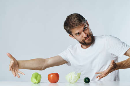 Man with a beard on a light background at a table showing vegetables, diet, vegetarianism.の写真素材