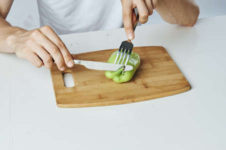 Man on a white background at the table cuts white pepper on a cutting board, diet, vegetarianism.