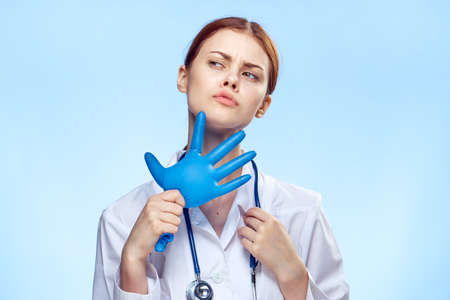 Beautiful young woman on a blue background in a medical dressing gown holds a puffed rubber glove, doctor, medicine.の写真素材
