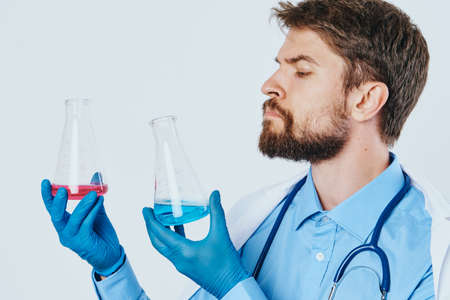 A man with a beard on a light background holds bottles for experiments, scientist, doctor, science, medicine.の写真素材