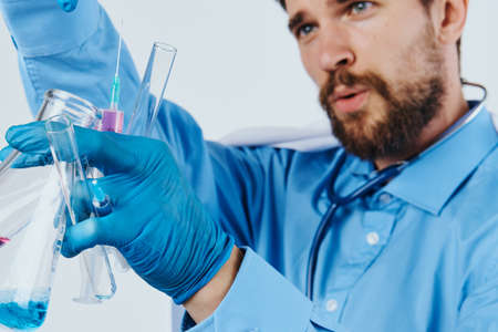 A man with a beard on a light background makes experiments with bottles in a medical dressing gown, medicine, scientist, science.の写真素材