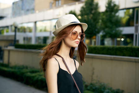 Young beautiful woman in sunglasses and in a white hat walking along the street in the city.の写真素材