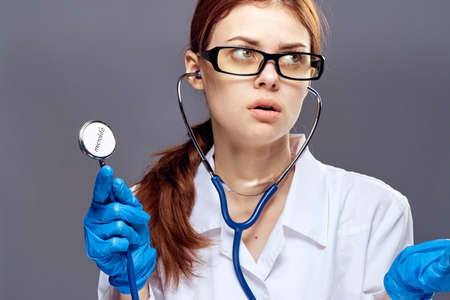 Young beautiful woman in medical gown holds a stethoscope on a gray backgroundの写真素材